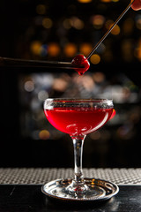 Putting a cocktail cherry on a glass with a drink, close up