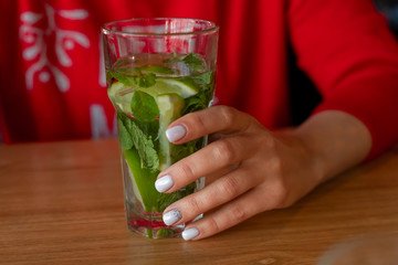 A glass of mineral water with lime, mint in the hands of a girl.  The concept of healthy drinks, detox.