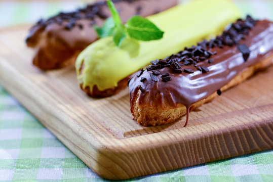 Traditional french dessert eclair pastry, three pieces laying on wooden board on a table covered with plaid fabric.