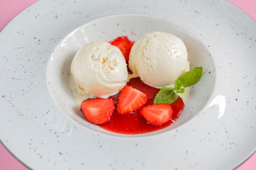 Vanilla strawberry ice cream with strawberry and fruit syrup in a white plate on pastel pink background. Top view.