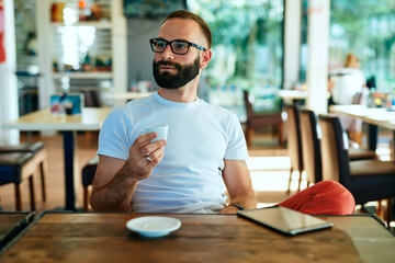 Young bearded man with glasses in a cafe working and having espresso coffee	