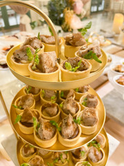 Beautifully decorated catering banquet table with small bites of snacks and appetizers with role of chicken served on golden plate.