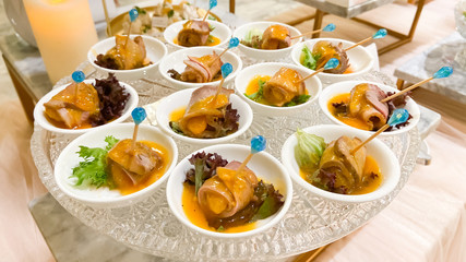 Beautifully decorated catering banquet table with small bites of snacks and appetizers on glass plate.