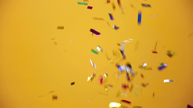 Flying falling down colorful golden glitter shimmer shine confetti isolated over yellow orange background in studio. Holiday party birthday lifestyle Happy New Year 2020 concept. Mock up copy space.