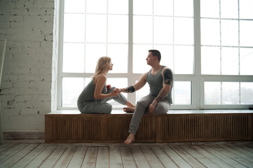 The concept of the february 14th. Loving couple on the windowsill near a large window and copy space. Loving couple with tattoos in a gray suit hugs near the window. Mody tone