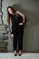 Full-length photo of a pretty brunette girl with excellent make-up in dark clothes standing on a gray background in a luxury vintage interior. The concept of a glamorous portrait.