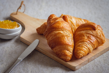 Fresh croissants on wooden board and orange jam in bowl