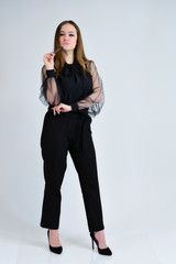 Concept portrait for a banner. A full-length photo of a pretty smiling girl A brunette girl with excellent makeup in dark clothes is standing on a white background, talking with emotions.