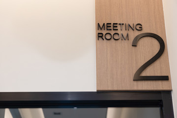 Vertically Light brown wood laminate label With embossed letters says word is "meeting room".