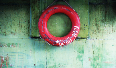 old red faded life buoy hanging on rusty with cracked paint metal green wall