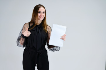 Concept portrait for a banner. A photo of a pretty smiling Brunette girl with a folder in her hands with excellent makeup in dark clothes is standing on a white background.