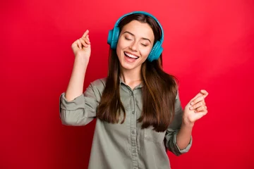 Tuinposter Photo of pretty lady cheerful mood modern technology headphones on ears listen new popular youth song wear casual grey green shirt isolated red color background © deagreez