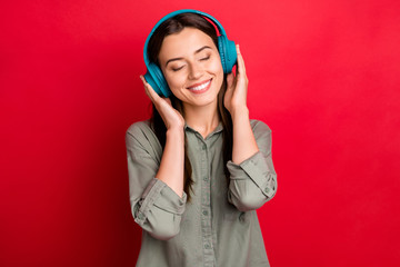 Photo of attractive lady cheerful mood holding hands on cool earflaps headphones listen new song eyes closed wear casual grey green shirt isolated red color background