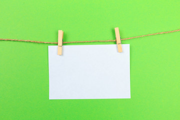 a piece of white paper attached to a rope clothespin on green background  - Image