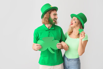 Young couple with shamrock on light background. St. Patrick's Day celebration