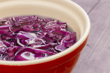 Sliced red cabbage soaking in water in a ceramic bowl.  With a wood background.