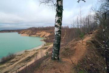 Obraz premium On the crest of the hill there is a path among the trees on the Bank of a sand quarry.