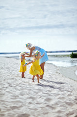Fototapeta na wymiar Happy family relaxing by the sea. Happy family resting at beach in summer.Young mother and her adorable little daughters on beach vacation. Concept of summer,childhood and leisure
