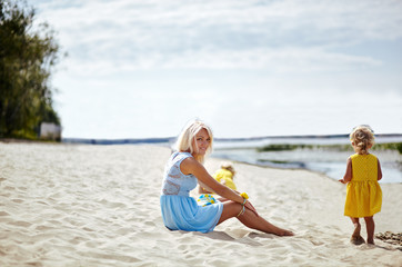Fototapeta na wymiar Happy family relaxing by the sea. Happy family resting at beach in summer.Young mother and her adorable little daughters on beach vacation. Concept of summer,childhood and leisure