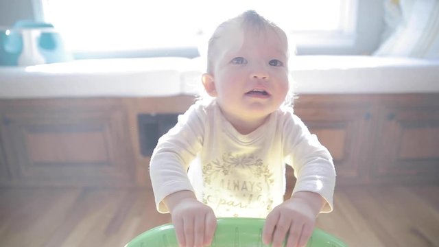One year old baby just learning how to walk, practicing first steps with a push toy walker.