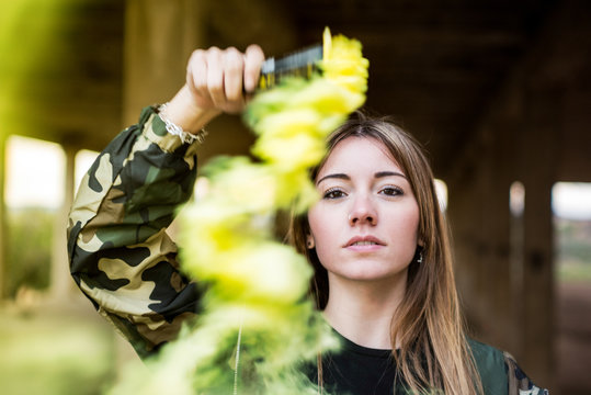 Brown hair girl holds a smoke bomb that throws yellow smoke around. Young girl wears an urban style, military jacket and piercing.