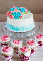 Festive cake with cream roses and multilayer dessert with fruit and cream cheese in a glass jar on a light background