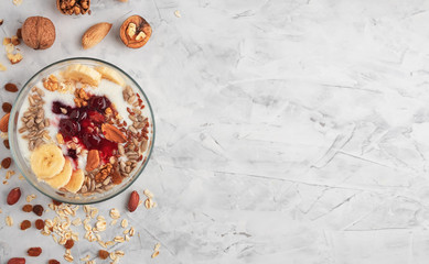 Healthy breakfast concept. Yogurt with granola, cherry jam and nuts in a cup on a gray background. Ingredients for breakfast on the table. Top view, horizontal orientation, copy space.
