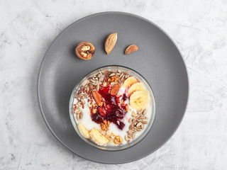 Healthy breakfast concept. Yogurt with granola, cherry jam and nuts, on a gray plate. Top view, horizontal orientation. Healthy natural food.
