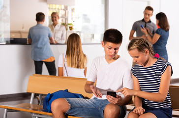 Girl and boy using phones, have rest between lessons
