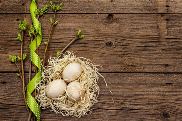 Zero waste Easter concept. Spring twigs with fresh green leaves, wooden eggs in nest, polka dot ribbon. Old vintage wooden boards background