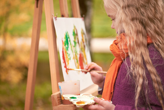 little girl artist paints autumn in the park