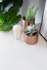 Bedroom working corner decorated with copper vase  with artificial plant inside and white candle in glass on cream spray-painted working table with  gray painted wall in the background /copy space