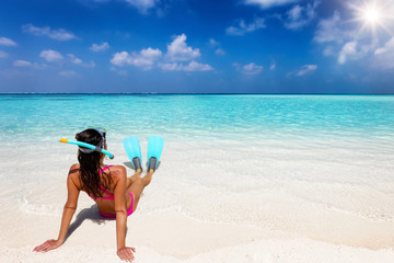Eine attraktive Frau im Bikini mit Taucherbrille und Flossen sitzt an einem tropischen Strand mit...