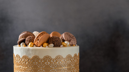 Chocolate cake decorated with candies and macaroons on dark background. Copy space, close up....