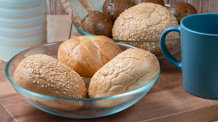 wheat buns with sesame filling in a glass bowl, a ceramic mug and a bottle of milk on the kitchen table.