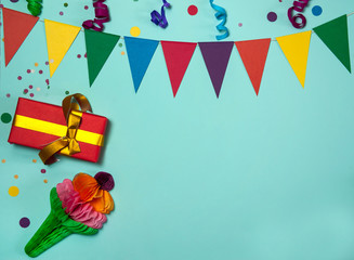 The concept of birthday. The border is made of a garland of colored paper flags, streamers, confetti and a gift box on a light blue background. Free space for your text.