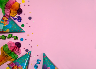 The concept of birthday. The border is made of cone caps, paper decorations, streamers and confetti on a pink background. Free space for your text.