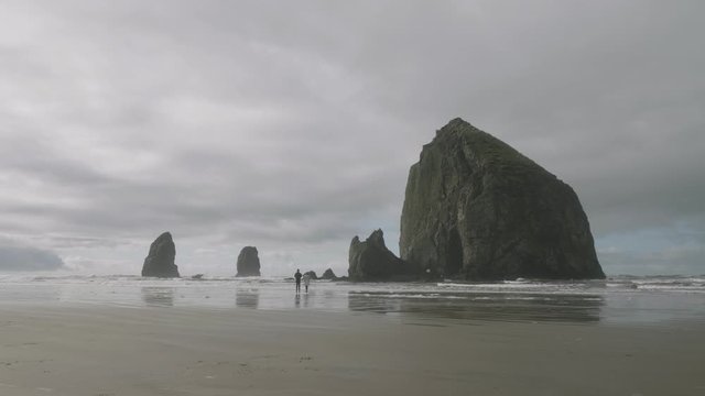 Couple people walking on sandy pacific ocean beach in front of huge haystack rock cliff at cannon beach oregon 