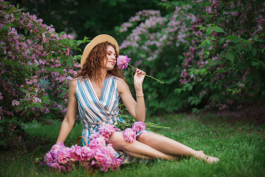 A pretty woman in spring garden with pink peonies bouquet in the basket breathes in the scent of flowers