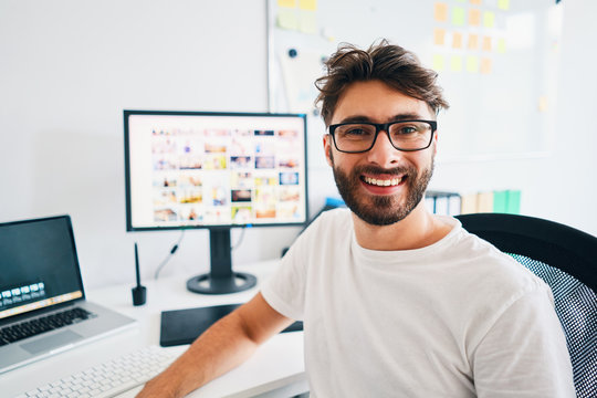 Portrait of photographer sitting in office and smiling at camera with portfolio in background