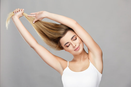 Beautiful Woman With Natural Make-up And Perfect Smile Pulling Up Her Healthy Blond Hair Wearing White Shirt