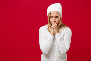 Young woman in white sweater, hat isolated on red wall background, studio portrait. Healthy fashion lifestyle, people emotions, cold season concept. Mock up copy space. Holding hands folded in prayer.