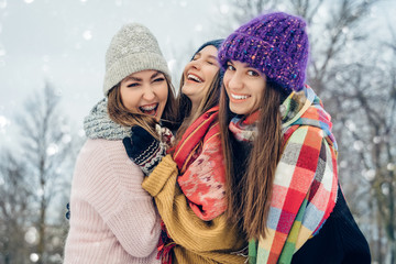 Three women friends outdoors in knitted hats having fun on a snowy cold weather. Group of young...