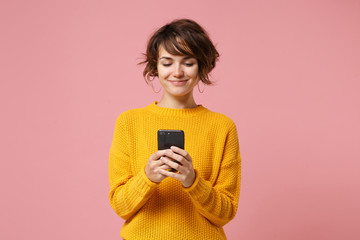 Smiling young brunette woman girl in yellow sweater posing isolated on pastel pink wall background...