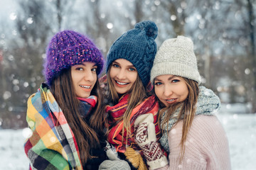 Three women friends outdoors in knitted hats having fun on a snowy cold weather. Group of young female friends outdoors in winter park.