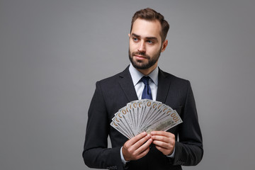 Handsome business man in suit shirt tie posing isolated on grey background. Achievement career wealth business concept. Mock up copy space. Hold fan of cash money in dollar banknotes, looking aside.