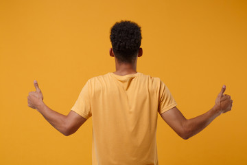 Back rear view of young african american guy in casual t-shirt posing isolated on yellow orange...
