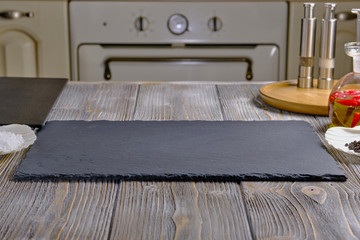 Rectangular plate of black color ardesia, on a wooden table. Spices on a wooden table. Red hot chili peppers in olive oil