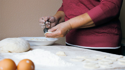 Mature female hands making dumplings with cheese at home kitchen.