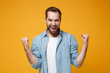 Joyful young bearded man in casual blue shirt posing isolated on yellow orange wall background,...
